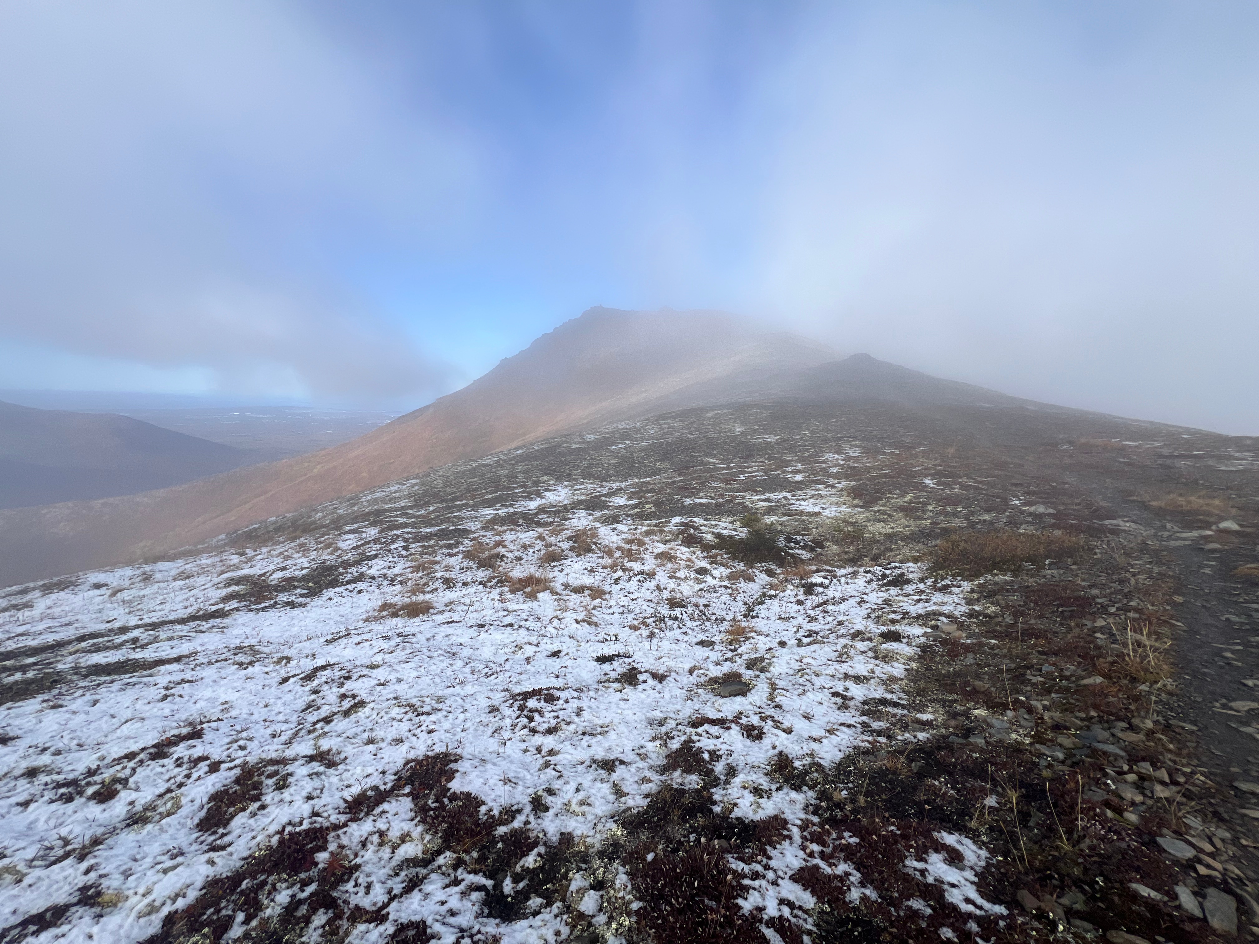The ridgeline rises back up towards Little Teton. It is foggy and there is a dusting of snow on the ground.