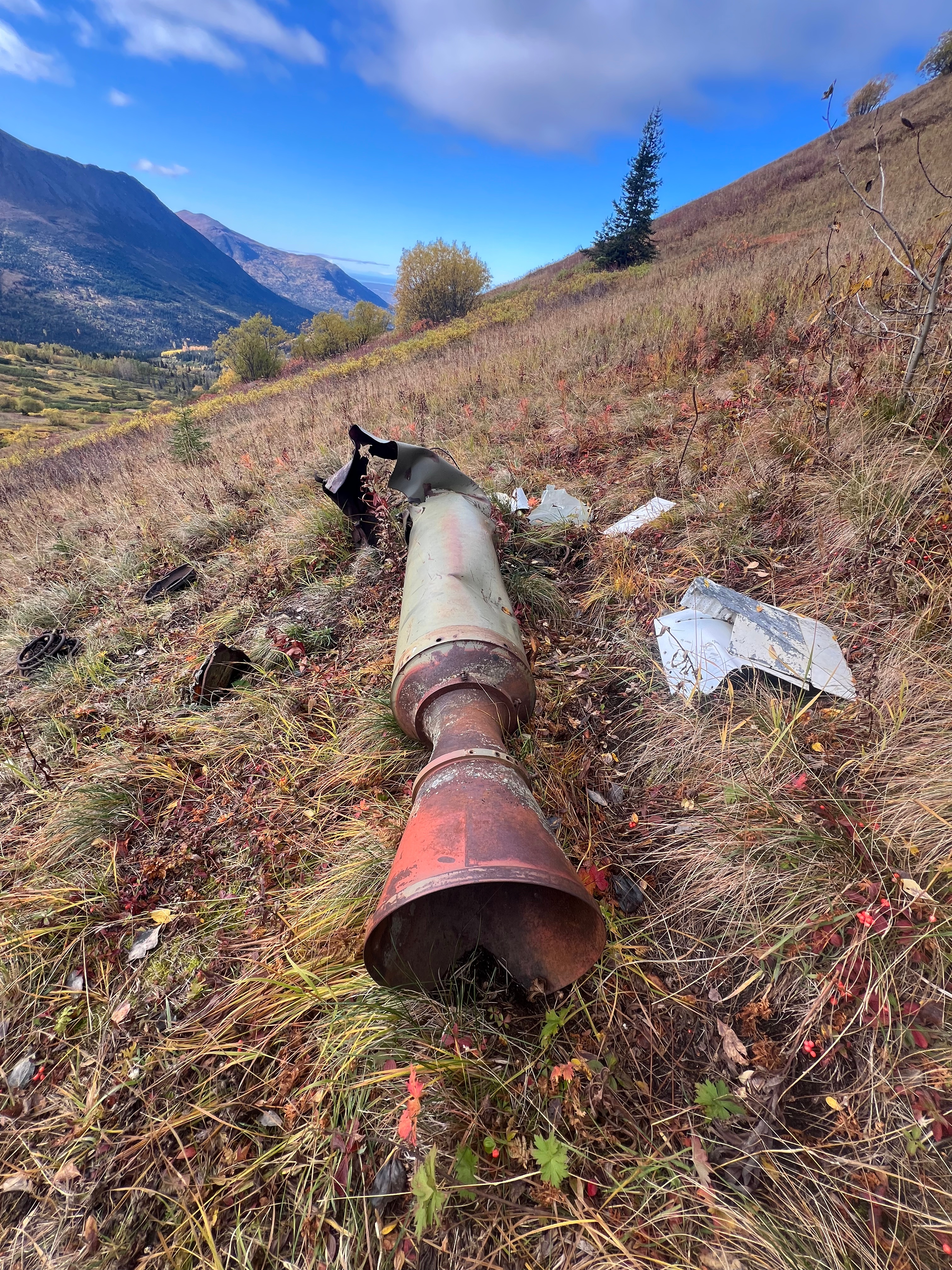 An old Nike Missile lays on the grass. The front end is destroyed. Parts and pieces are scattered about