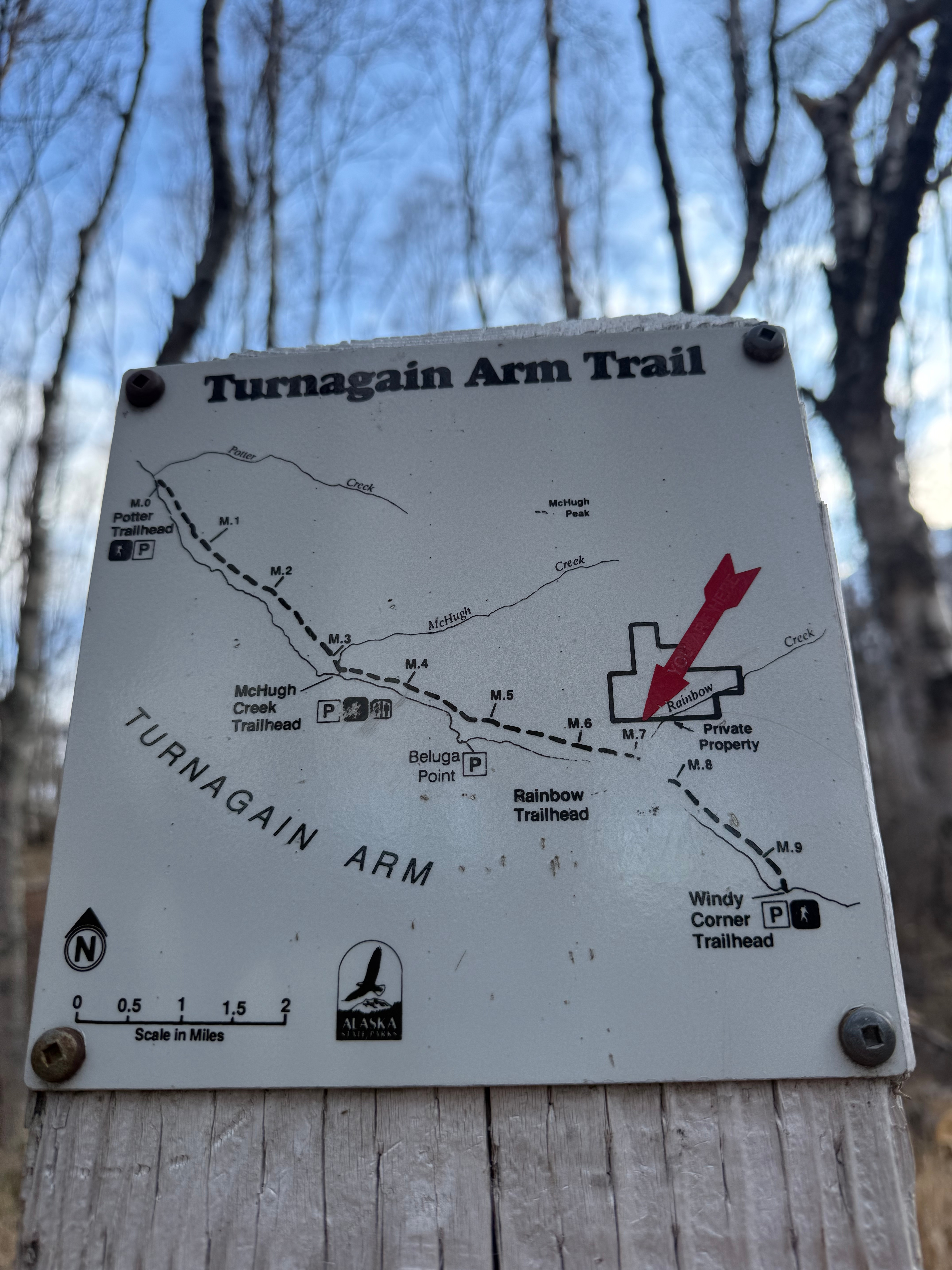 A small map on a wooden post with mileages of the Turnagain Arm Trail. A red arrow points to our location.