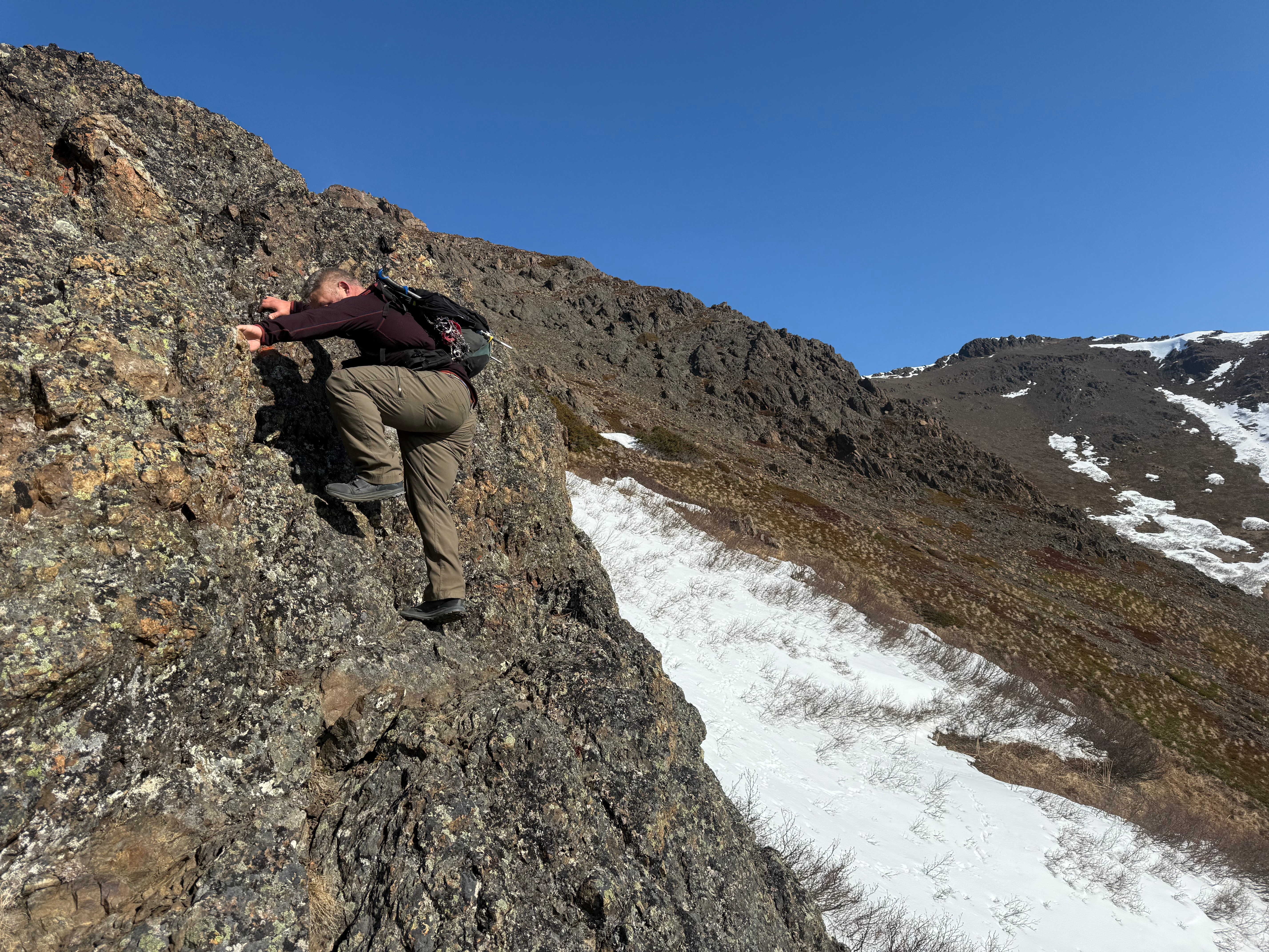 A hiker climbs up a vertical rock face.
