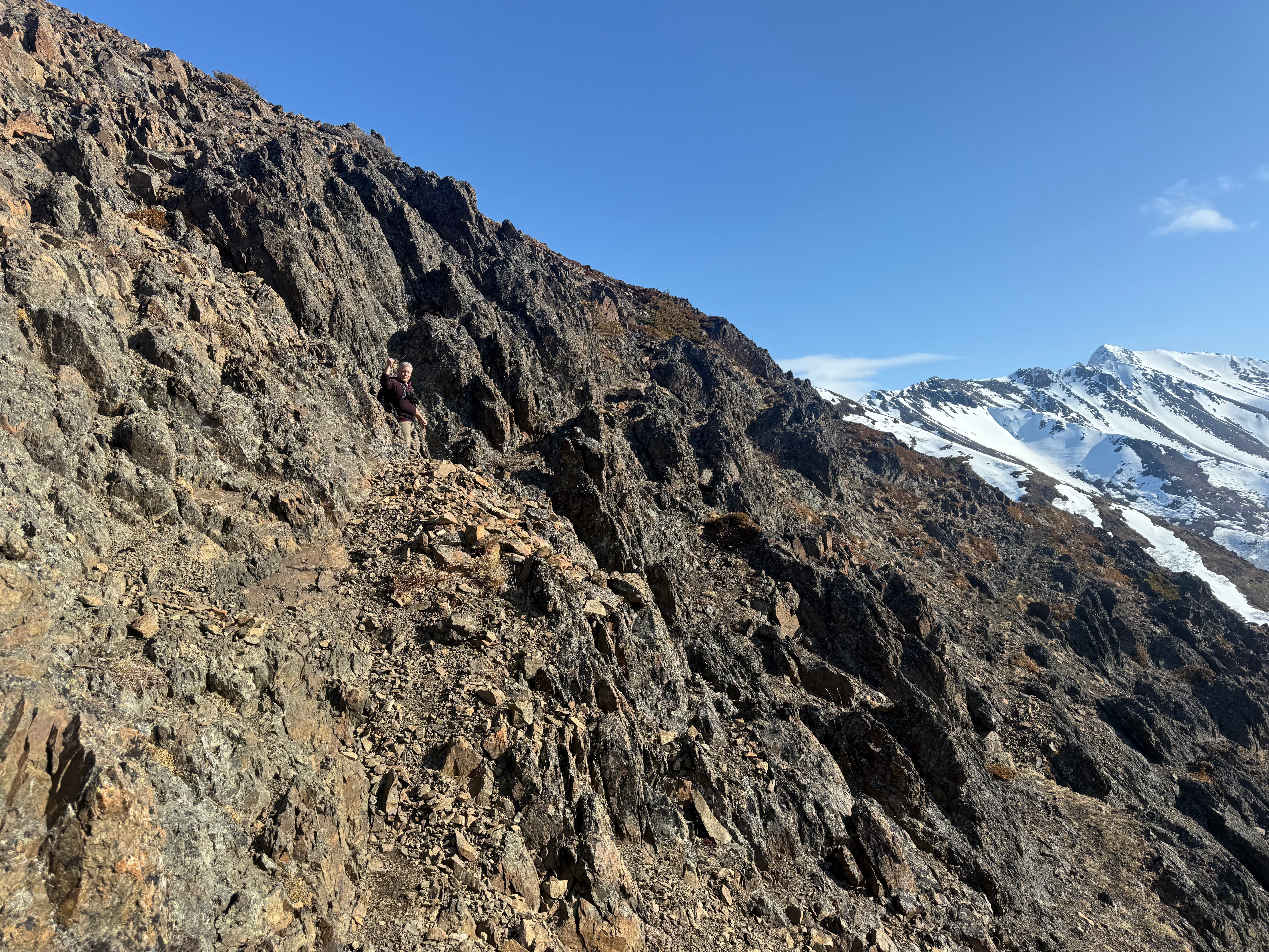 A hiker blends into the rocky, steep slope. The trail is narrow and rocky.