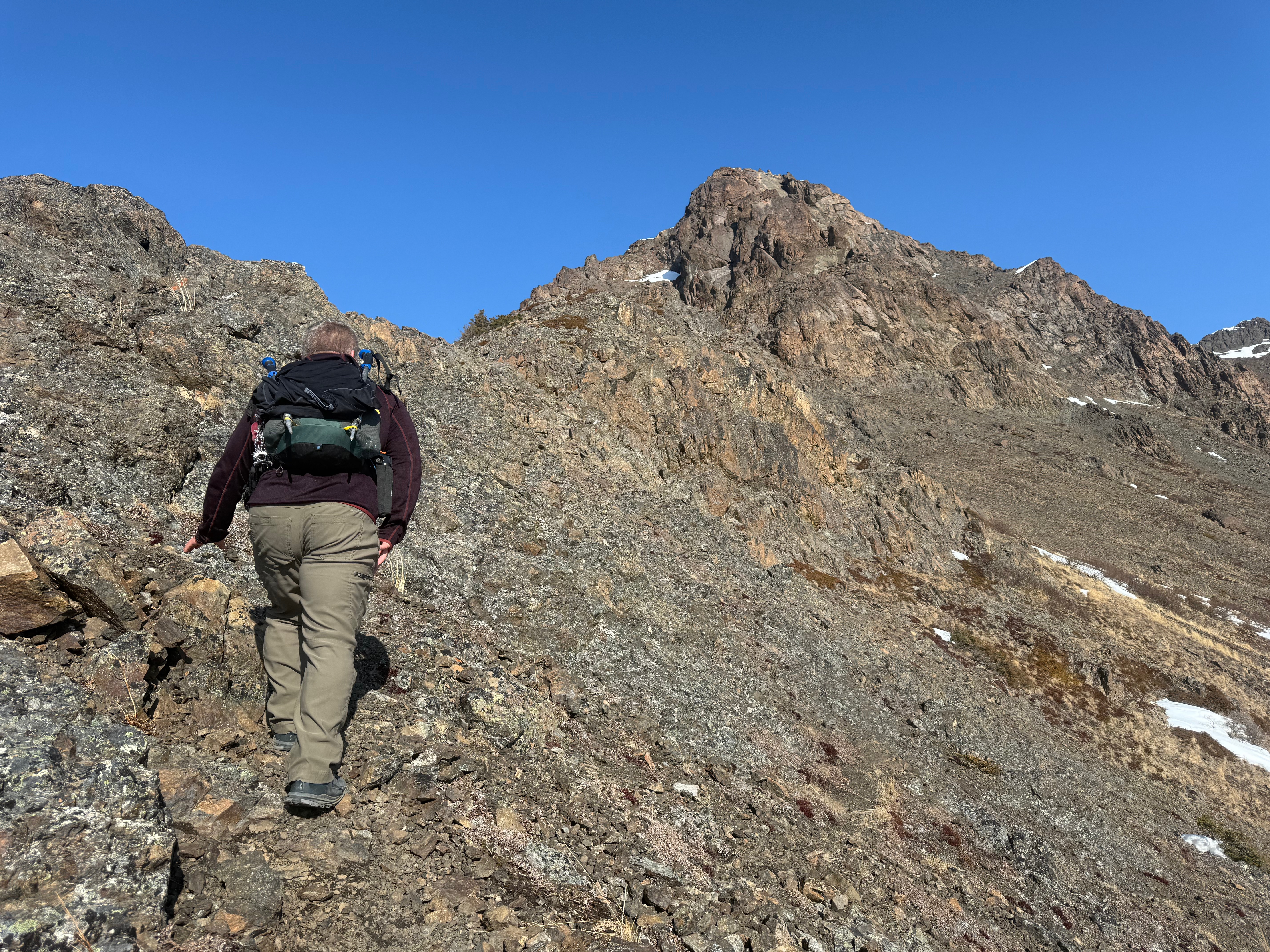 A hiker climbs up a rocky slope. The summit is not far above.