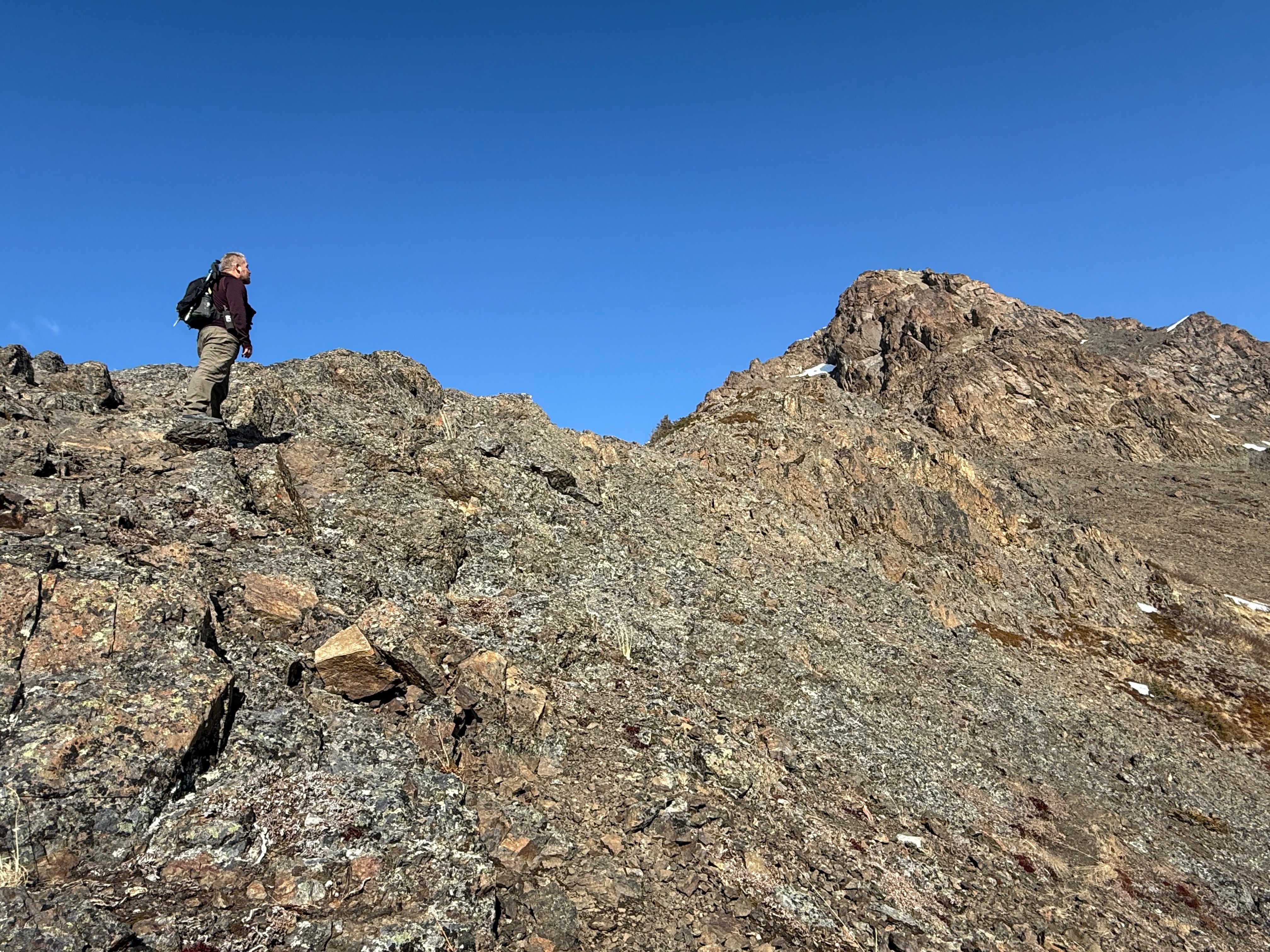 A hiker stands on a rock and looks up at the summit.