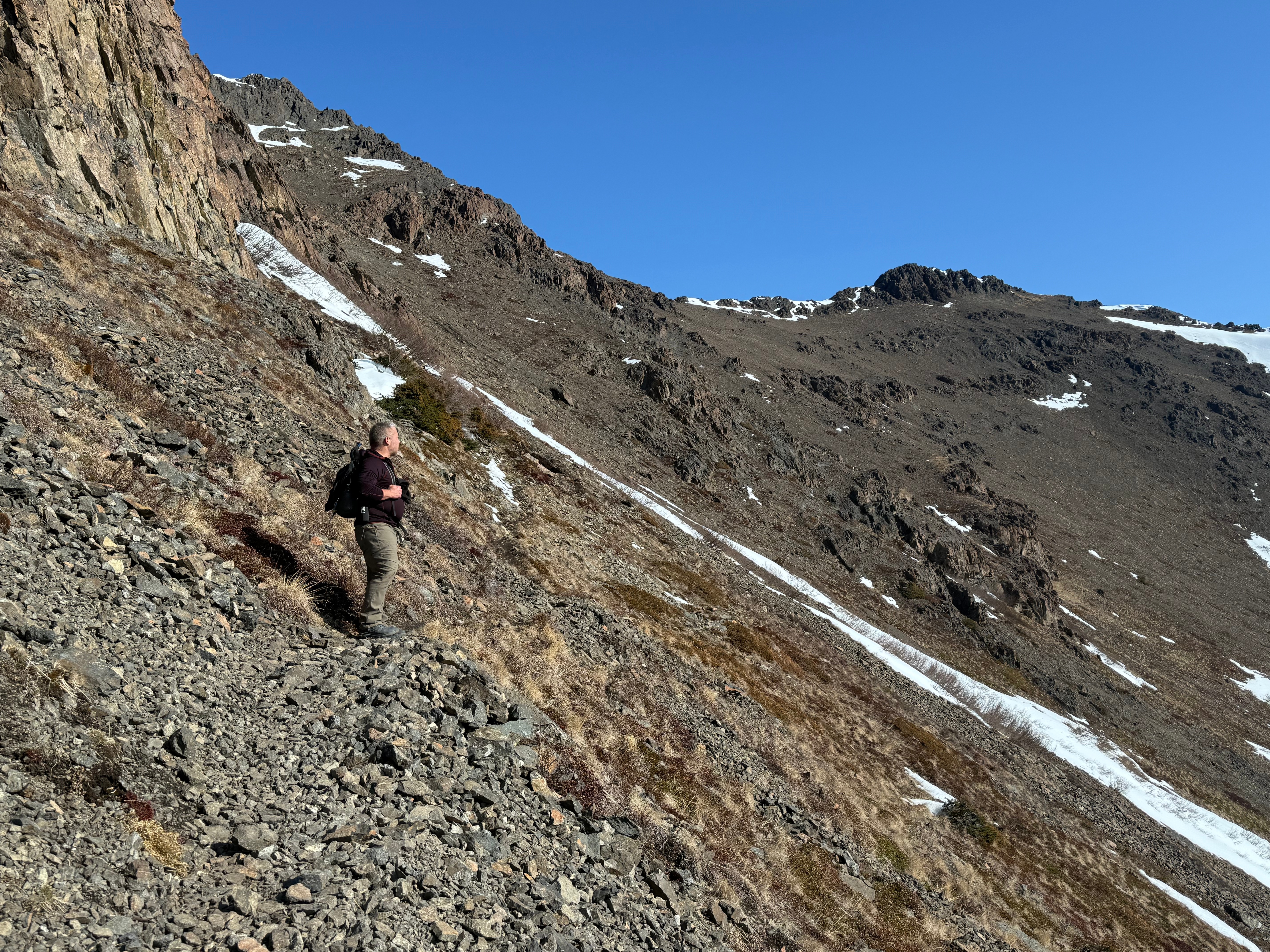 A hiker stand on a rocky section of the steep slope below the summit ridge,