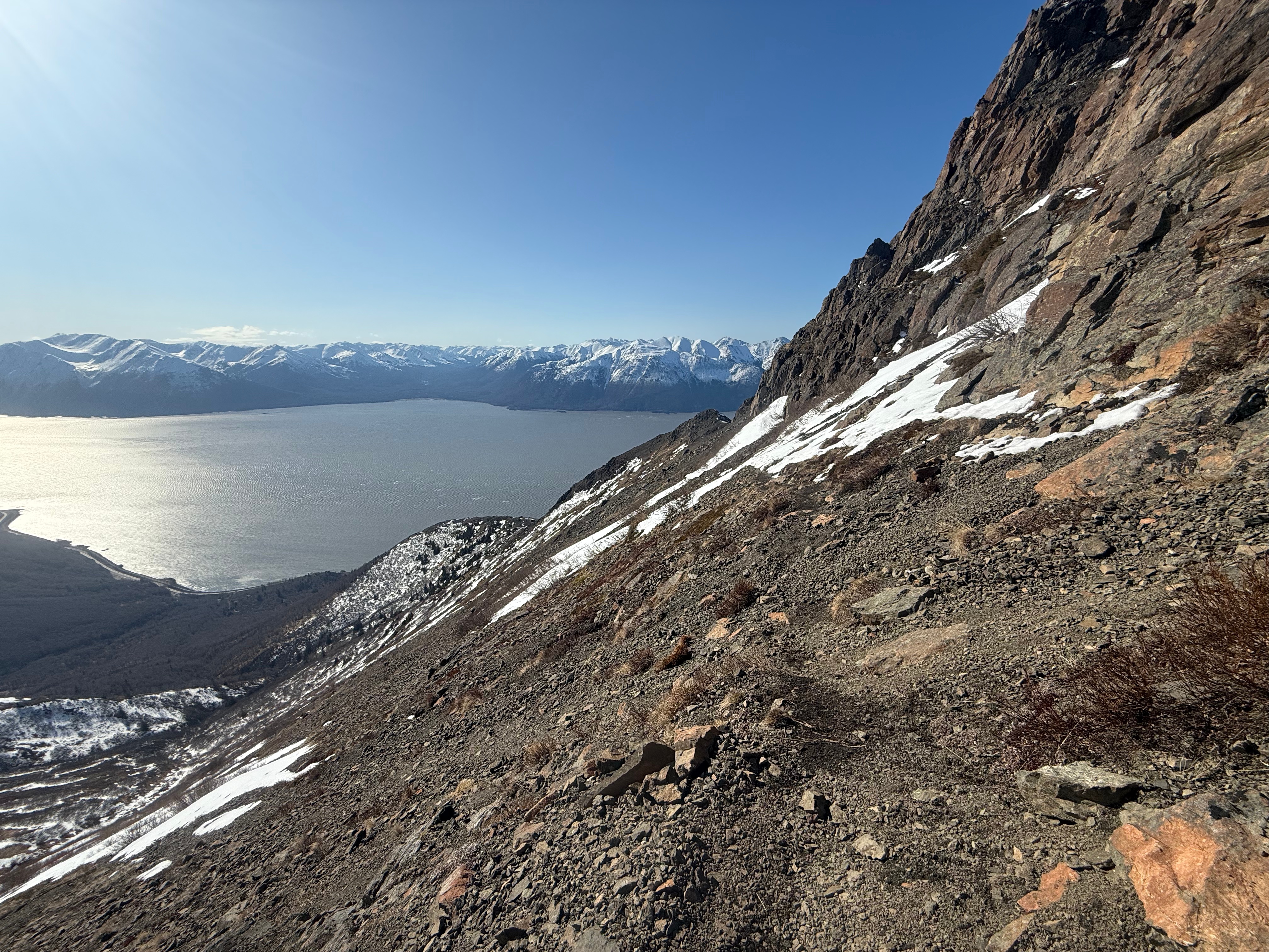 Facing back along the trail from the steep scree slope below the summit. The scree slope drops off steeply to the left and the ocean and highway are far below.