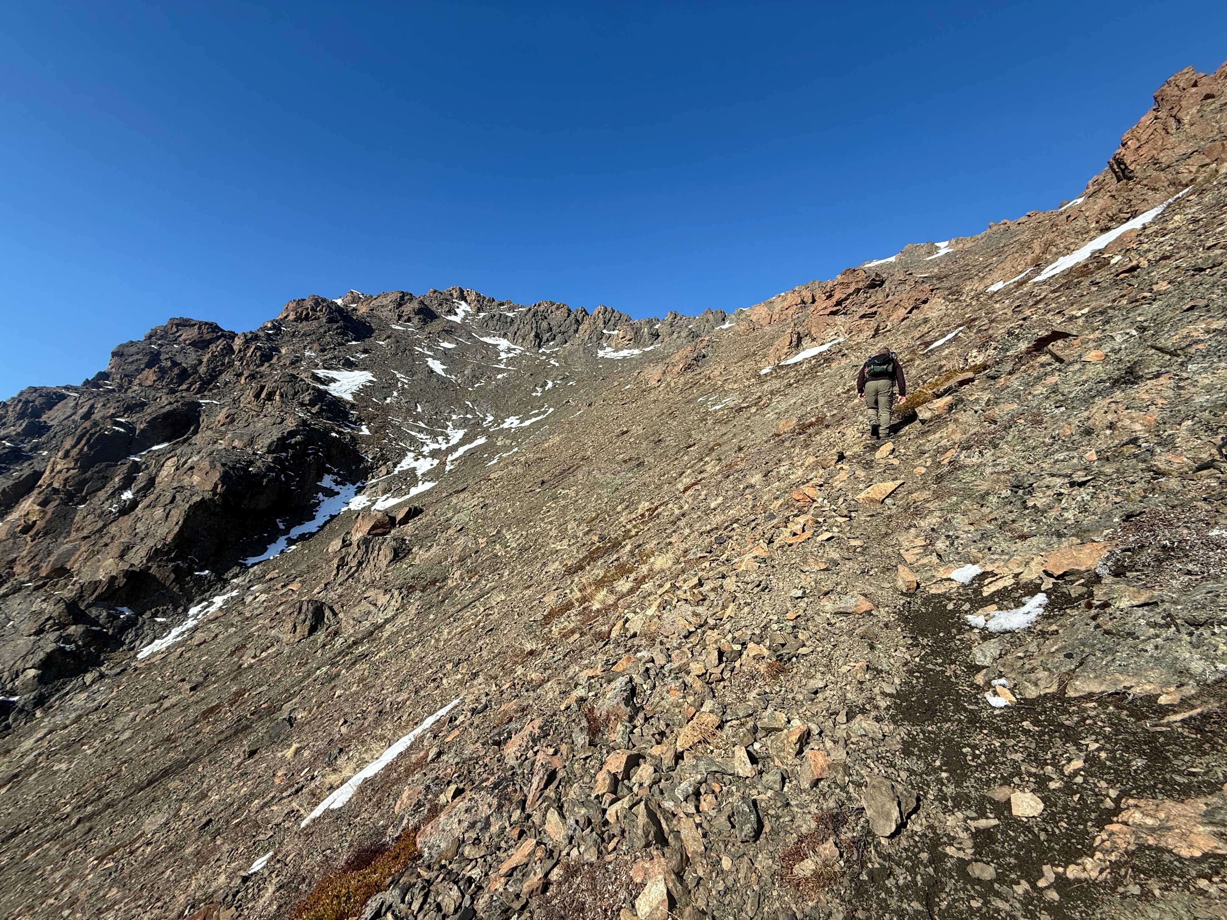 A hiker ascends a steep, rocky slope. The summit ridge is not far above.