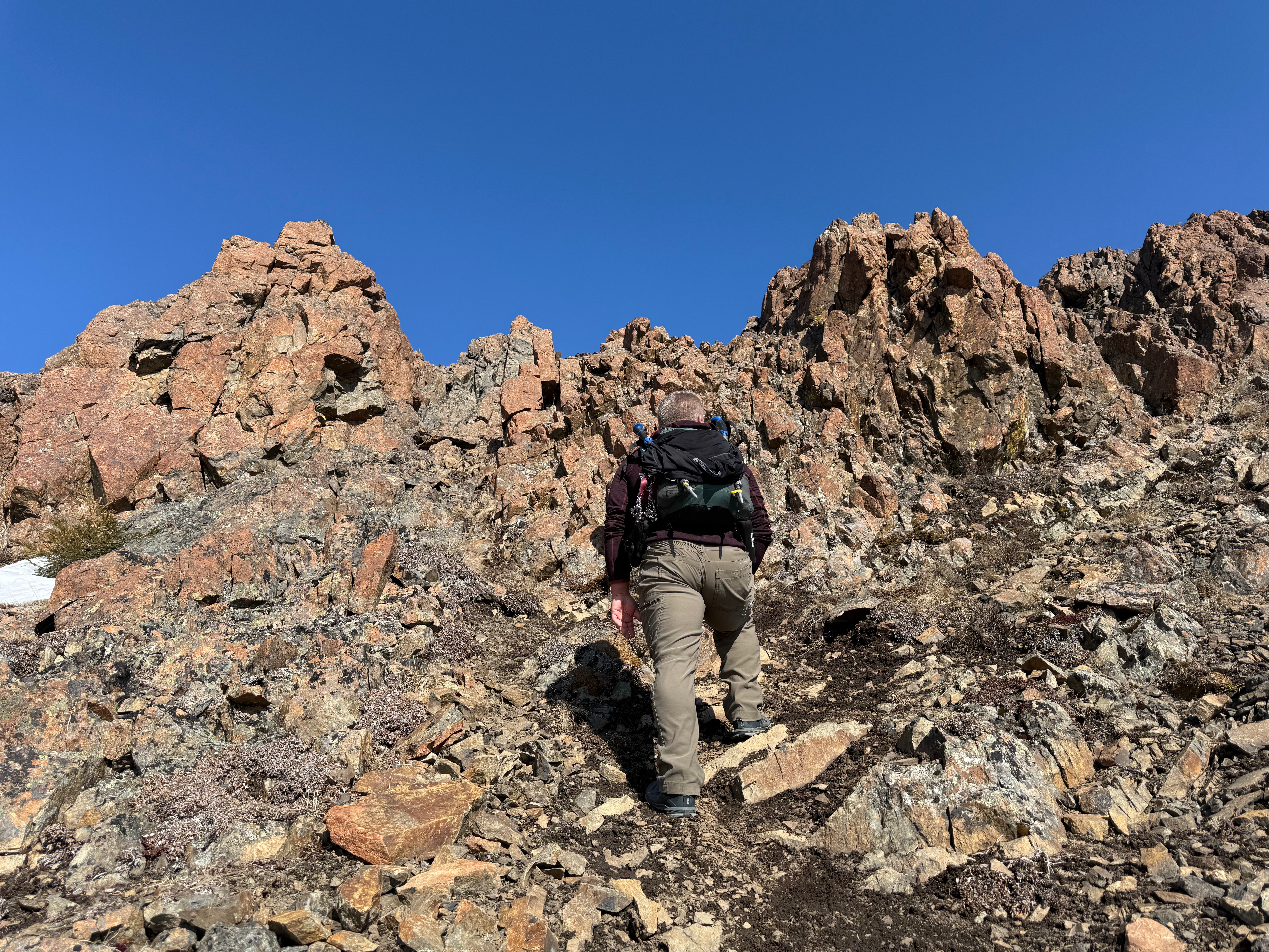 A hiker stands below a vertical, rocky slope.