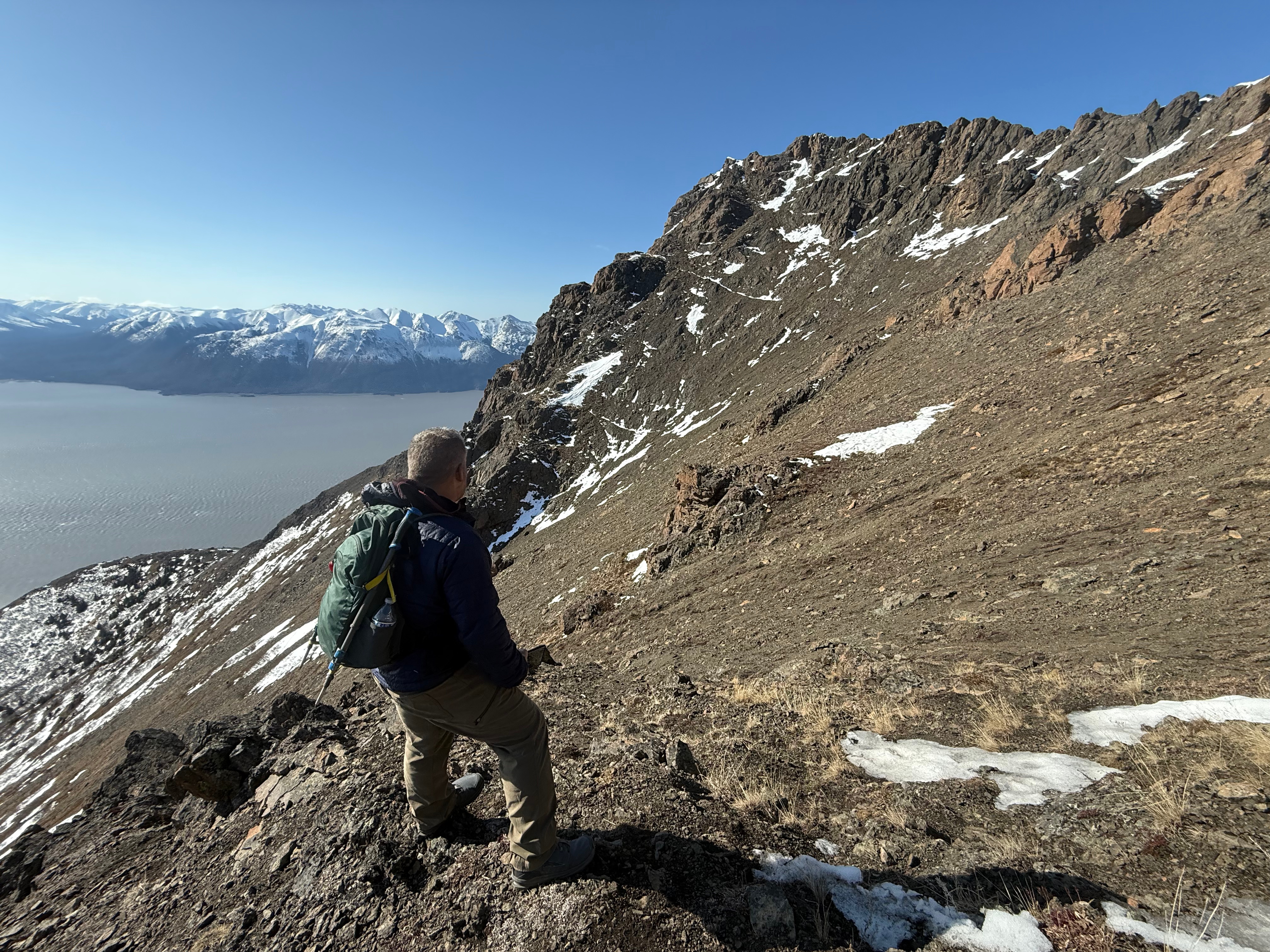 A hiker is standing on the scree slope just below the ridge facing towards the summit. The second step and the ocean are below.