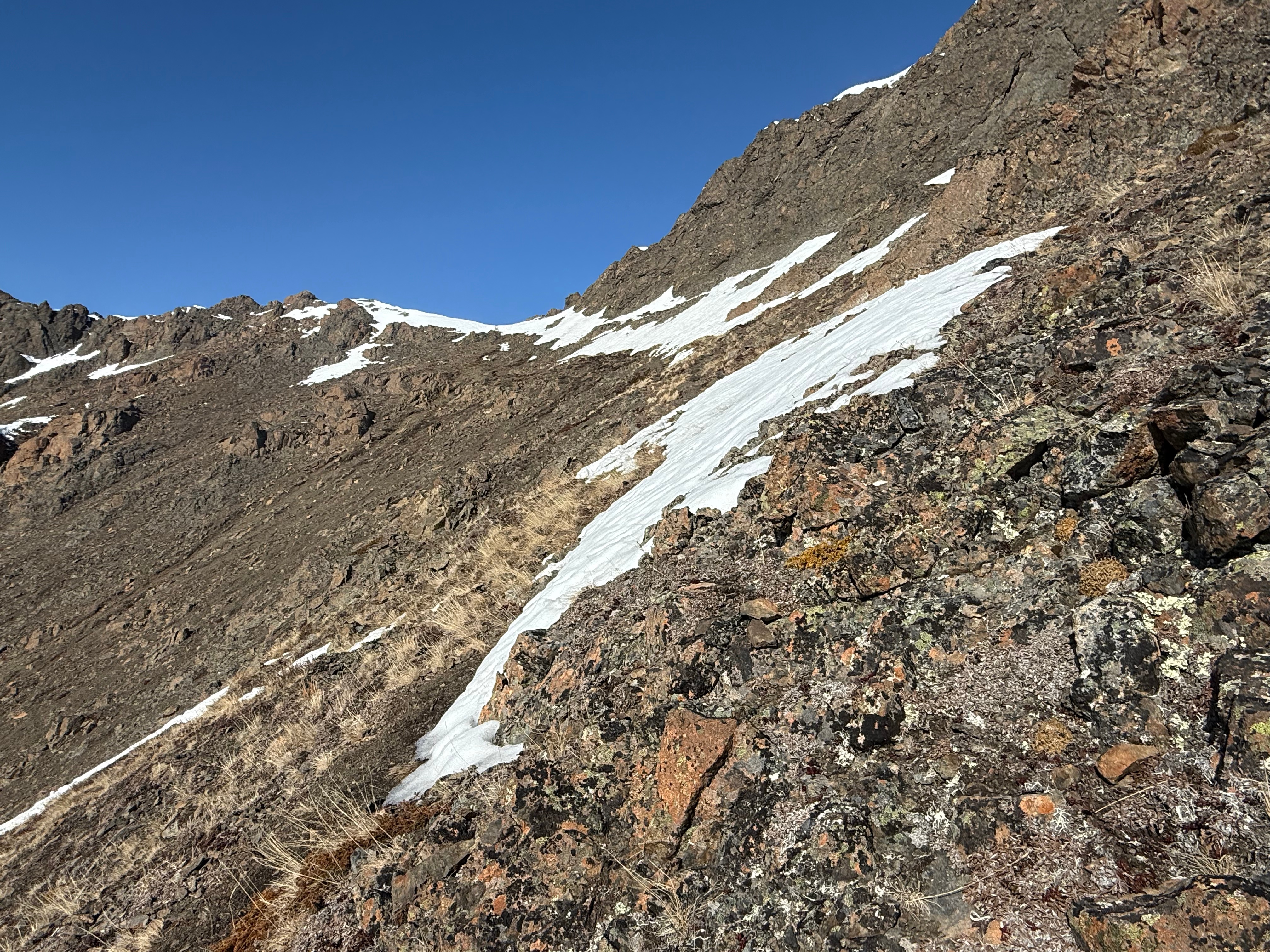 Snow dots the final stretch of the ascent of the scree slope leading to the summit ridge