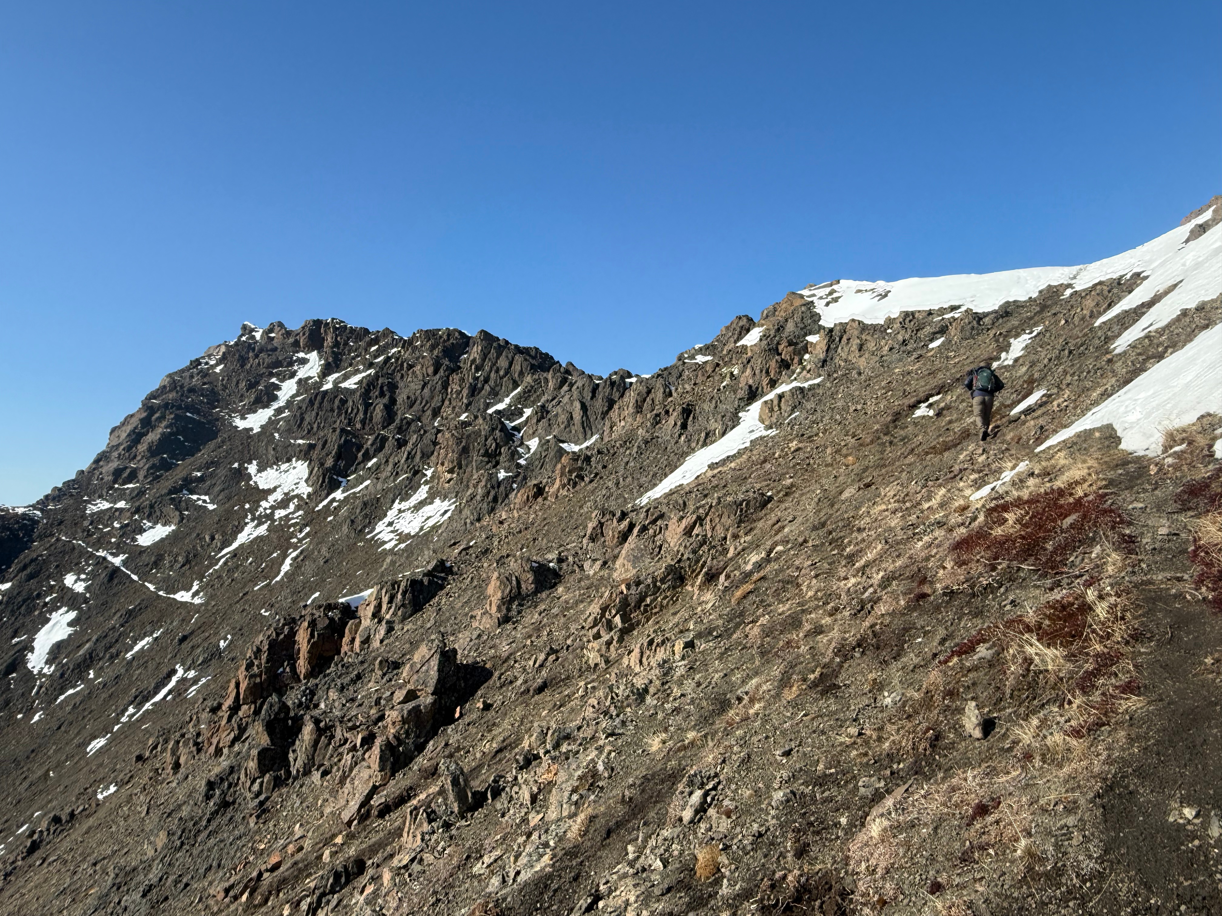 A hiker walking up the final feet to the summit ridge. Only a short section of snow to cross.
