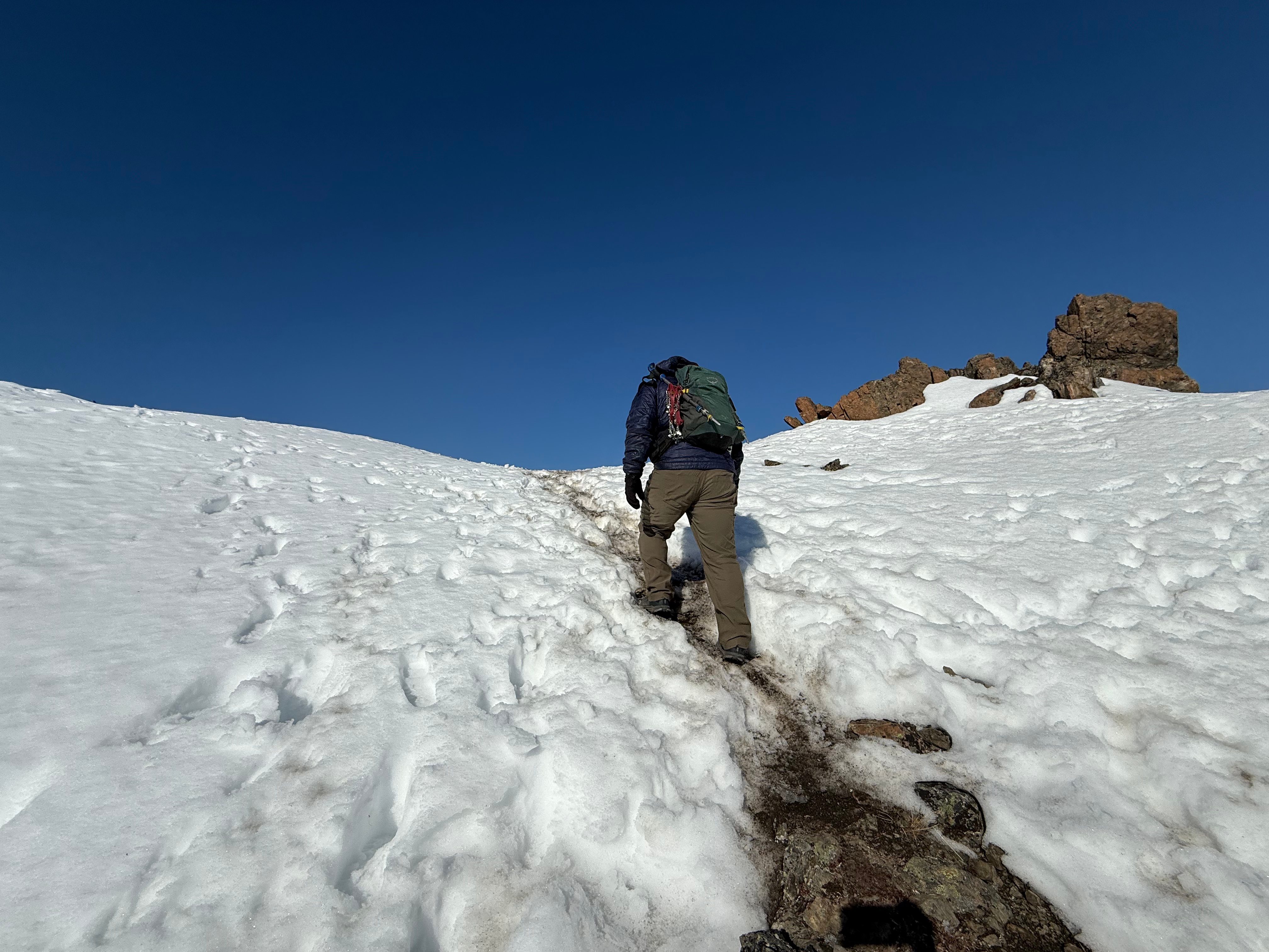 A hiker walking up the last snowy section before achieving the summit ridge.