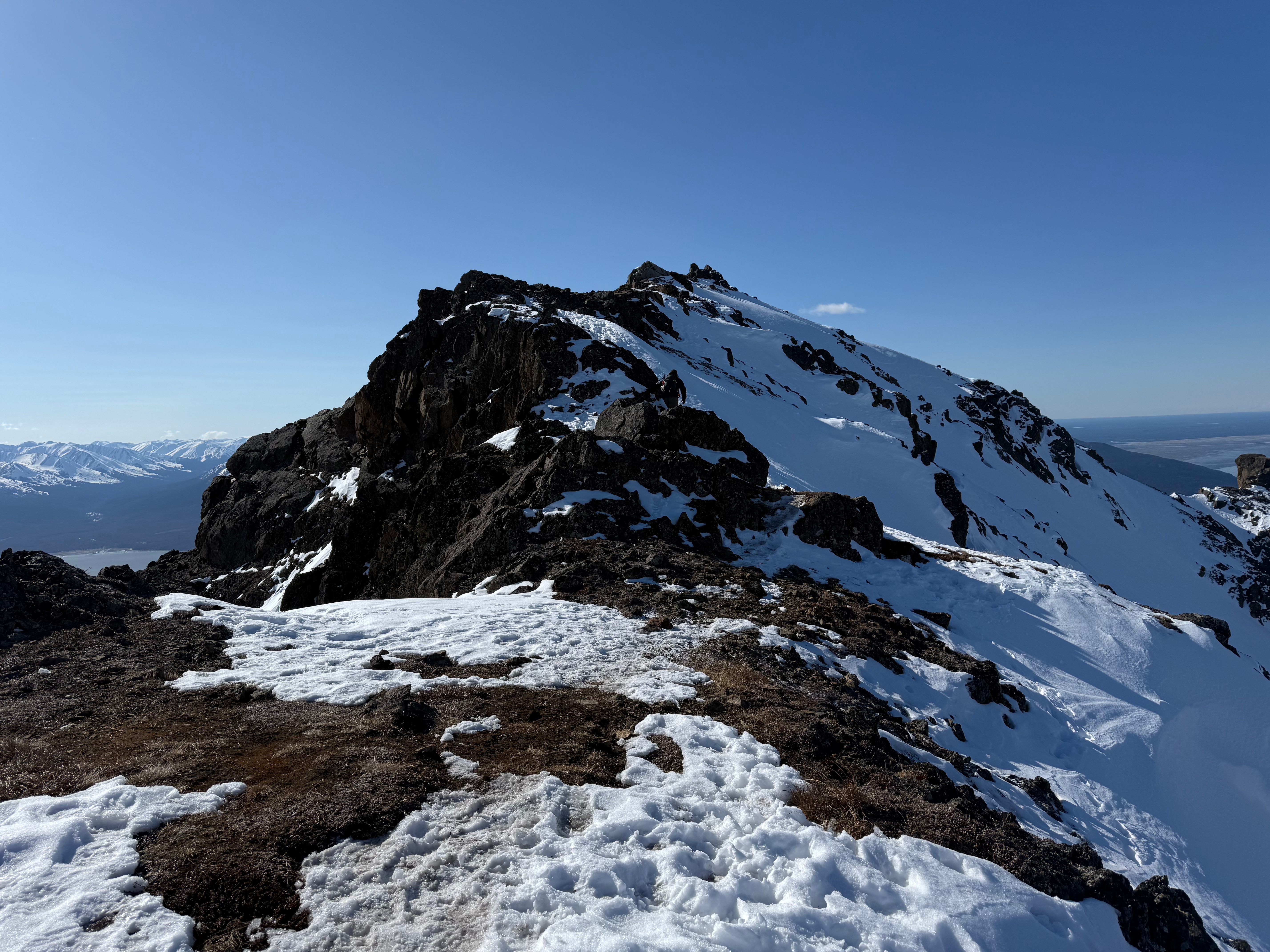 A hiker climbs the final snow and rocky feet to the summit.