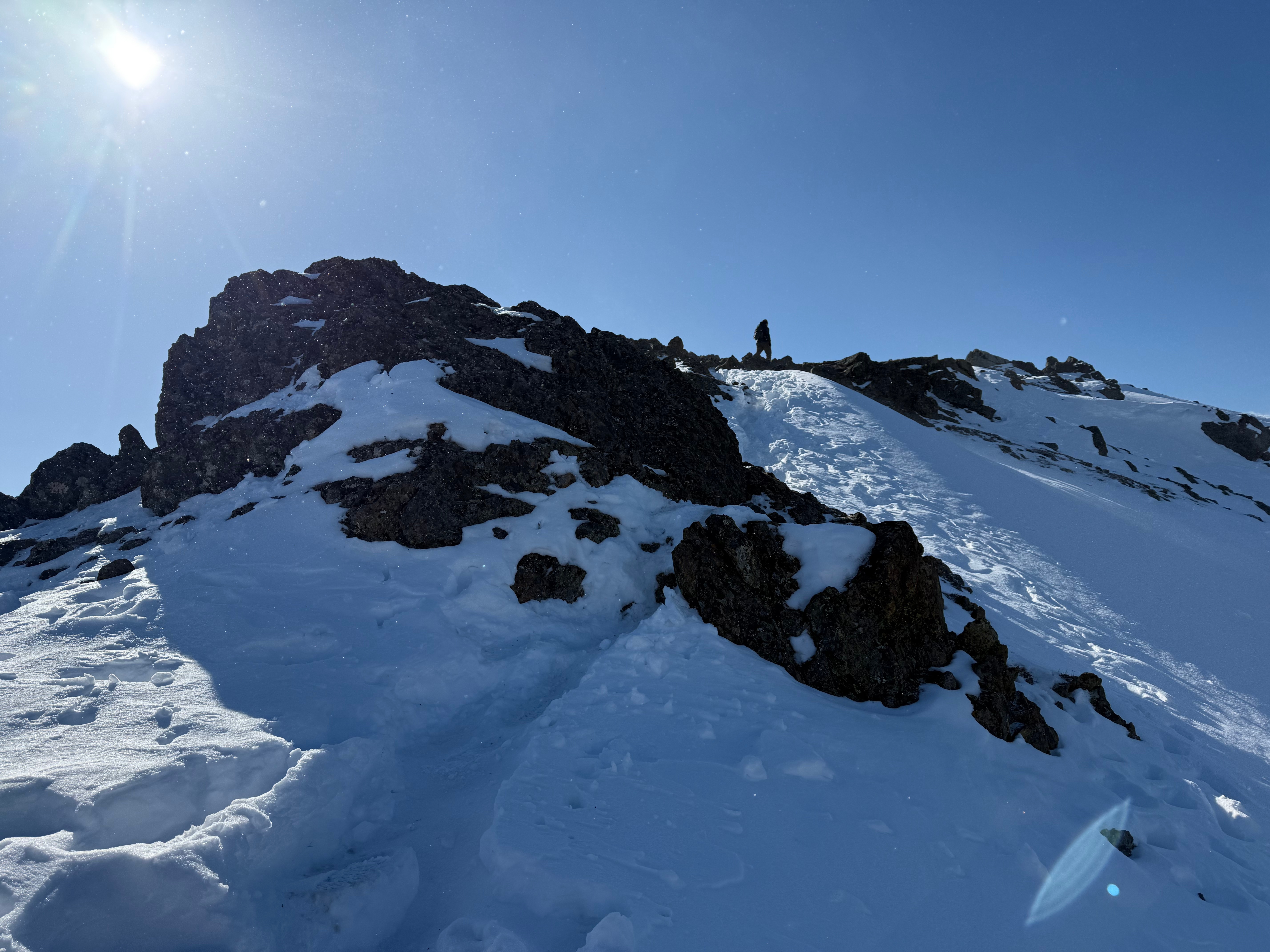 A hiker climbs the final snow and rocky feet to the summit.