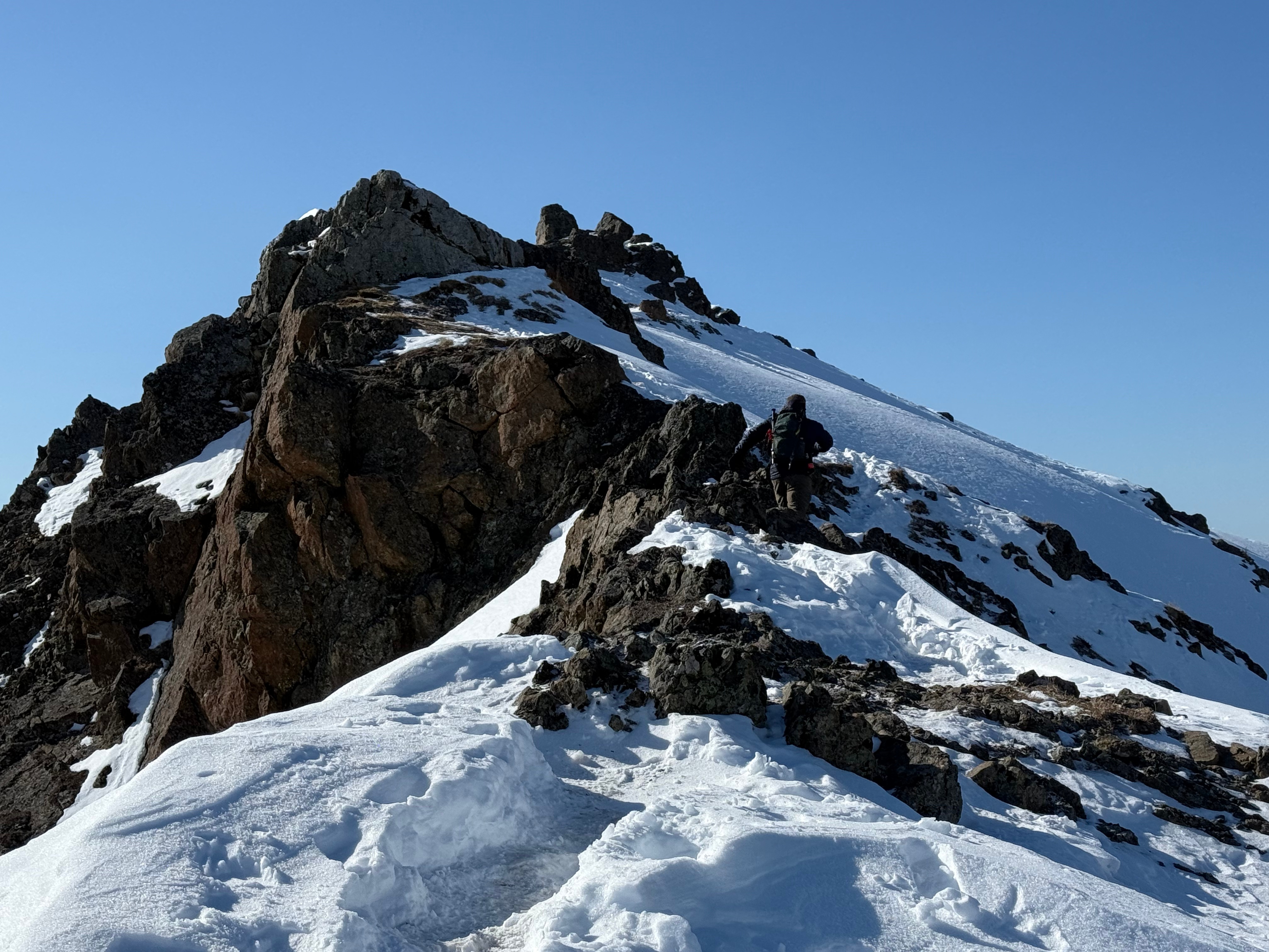 A hiker negotiates the final ascent to the summit. The trail is snow covered, but packed down from prior travelers.