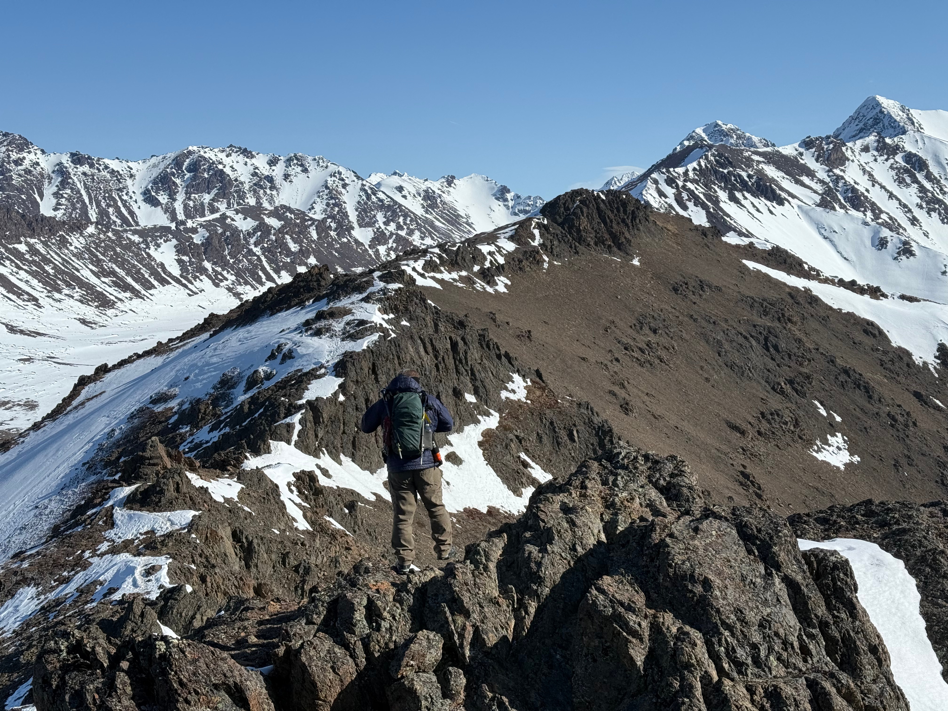 A hiker starts walking along the summit ridge towards a rocky bump at the far end of the top of the scree slope.