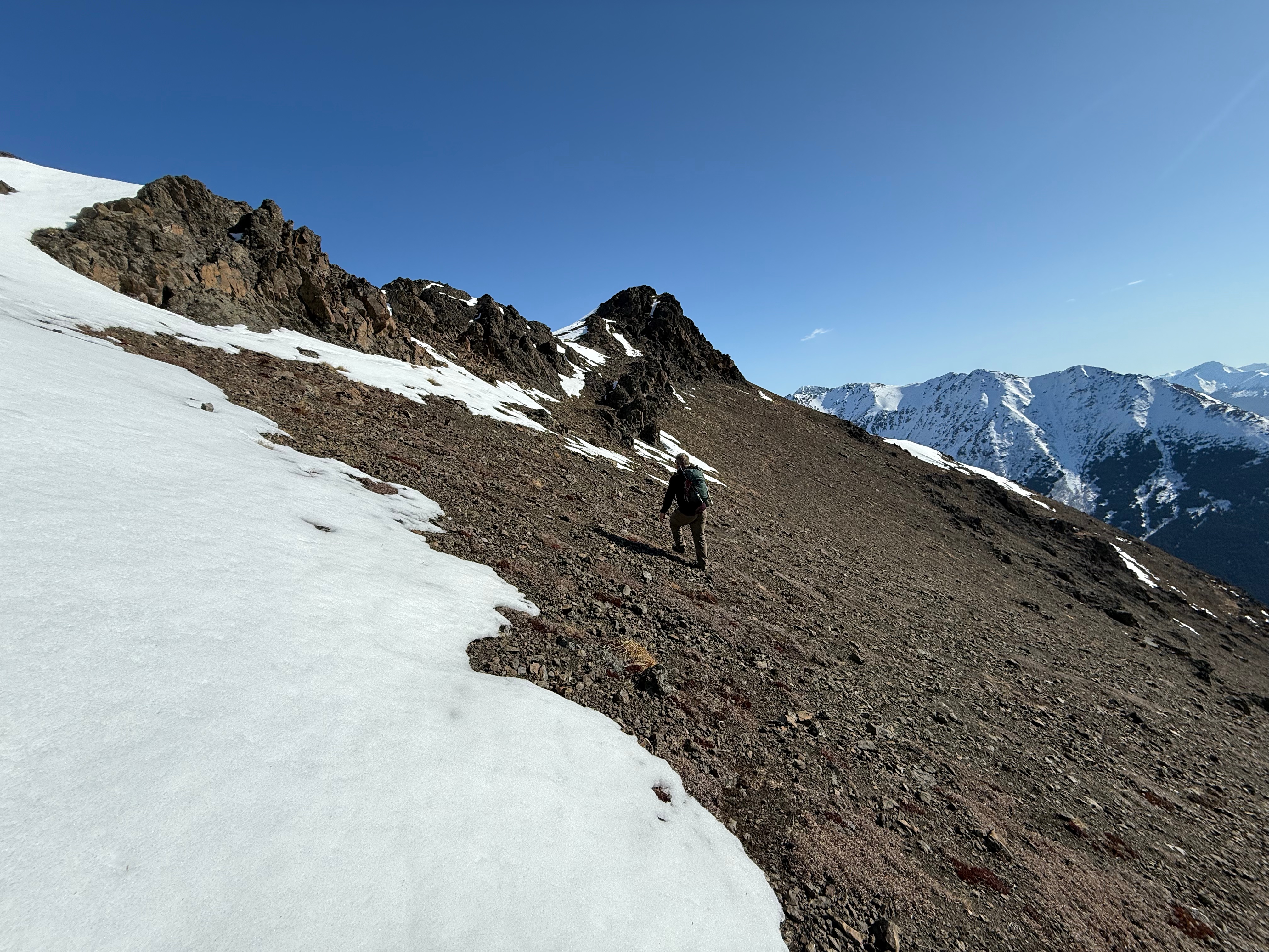 A hiker traverses the scree slope heading towards the bump on the ridge.