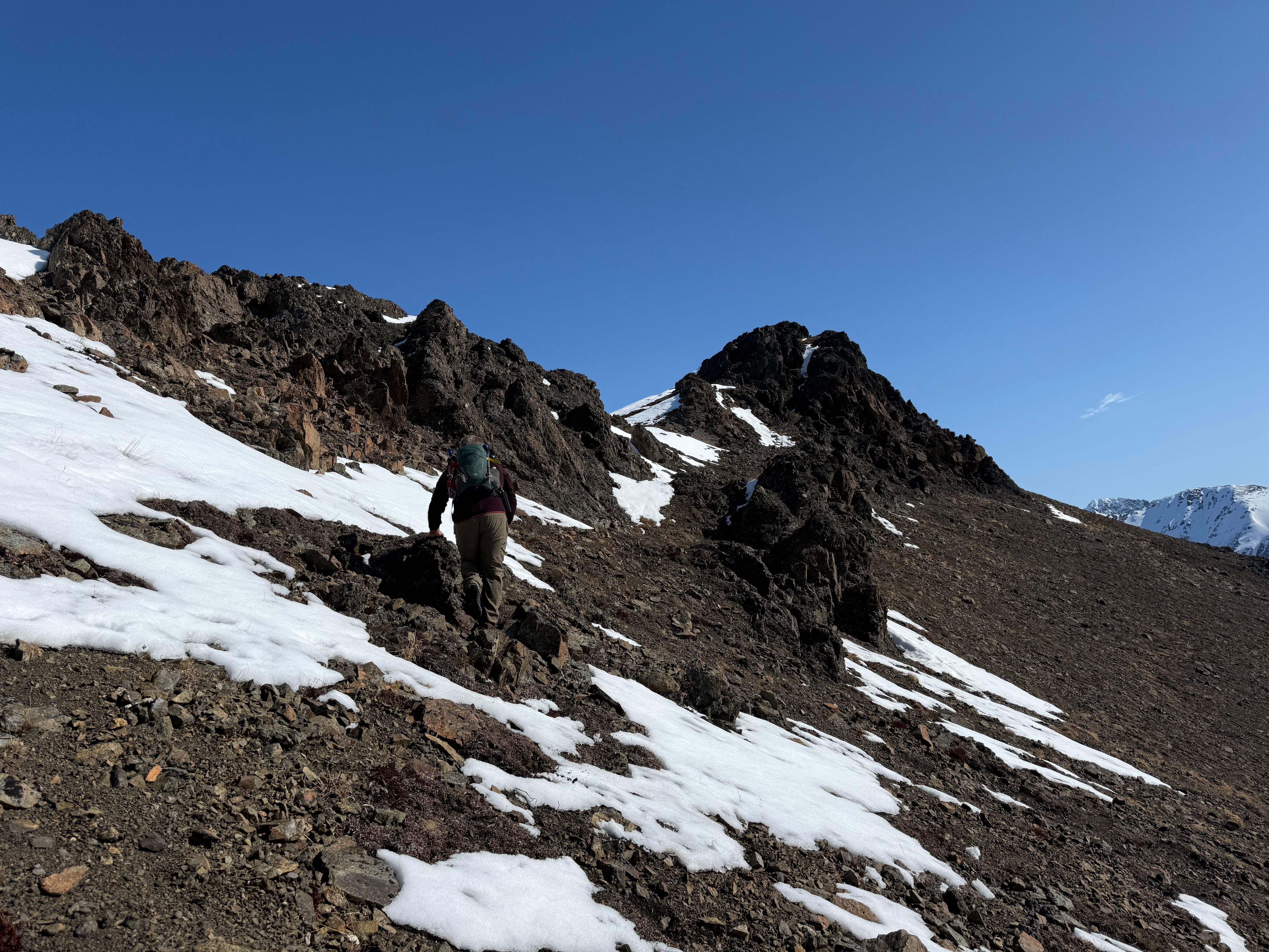 A hiker traverses the scree slope heading towards the bump on the ridge.