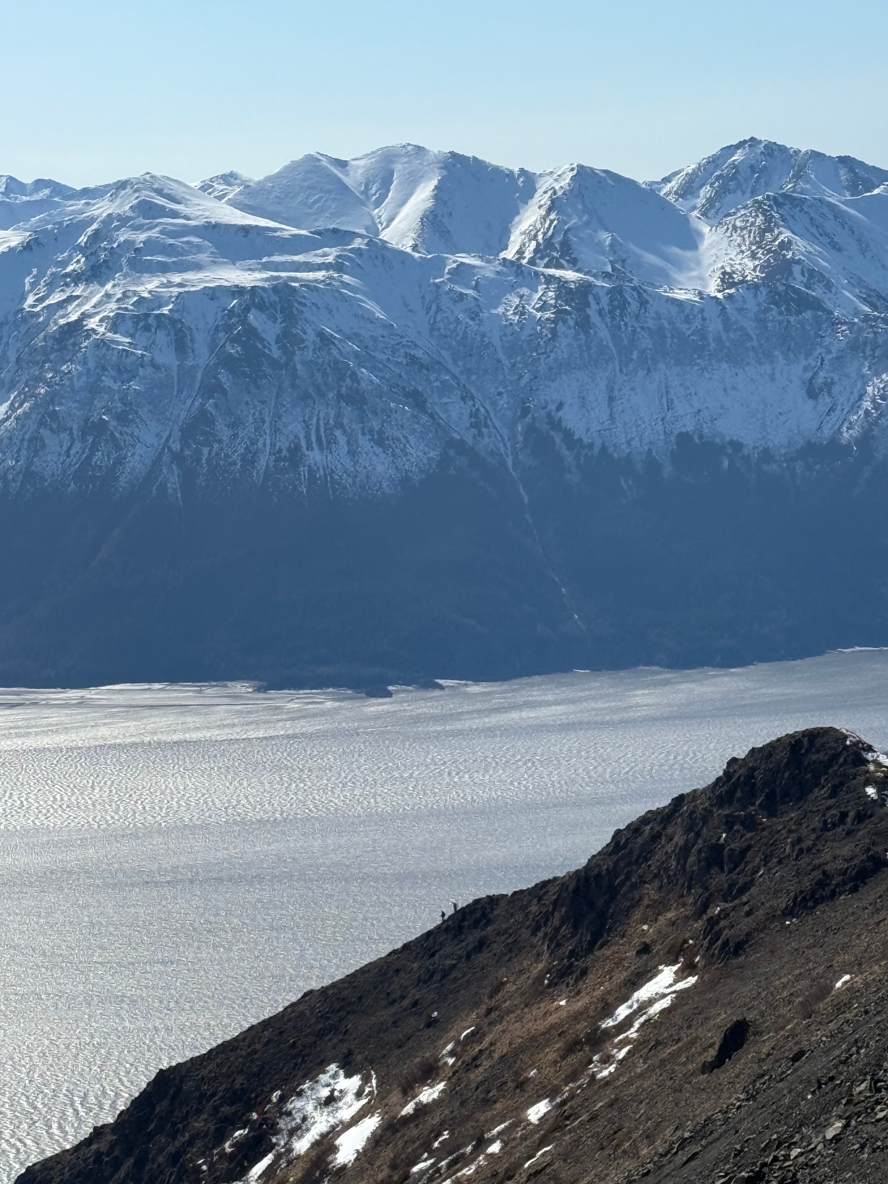Two hikers way off in the distance descending the second step. Mountains across the inlet rise up to snow capped peaks.