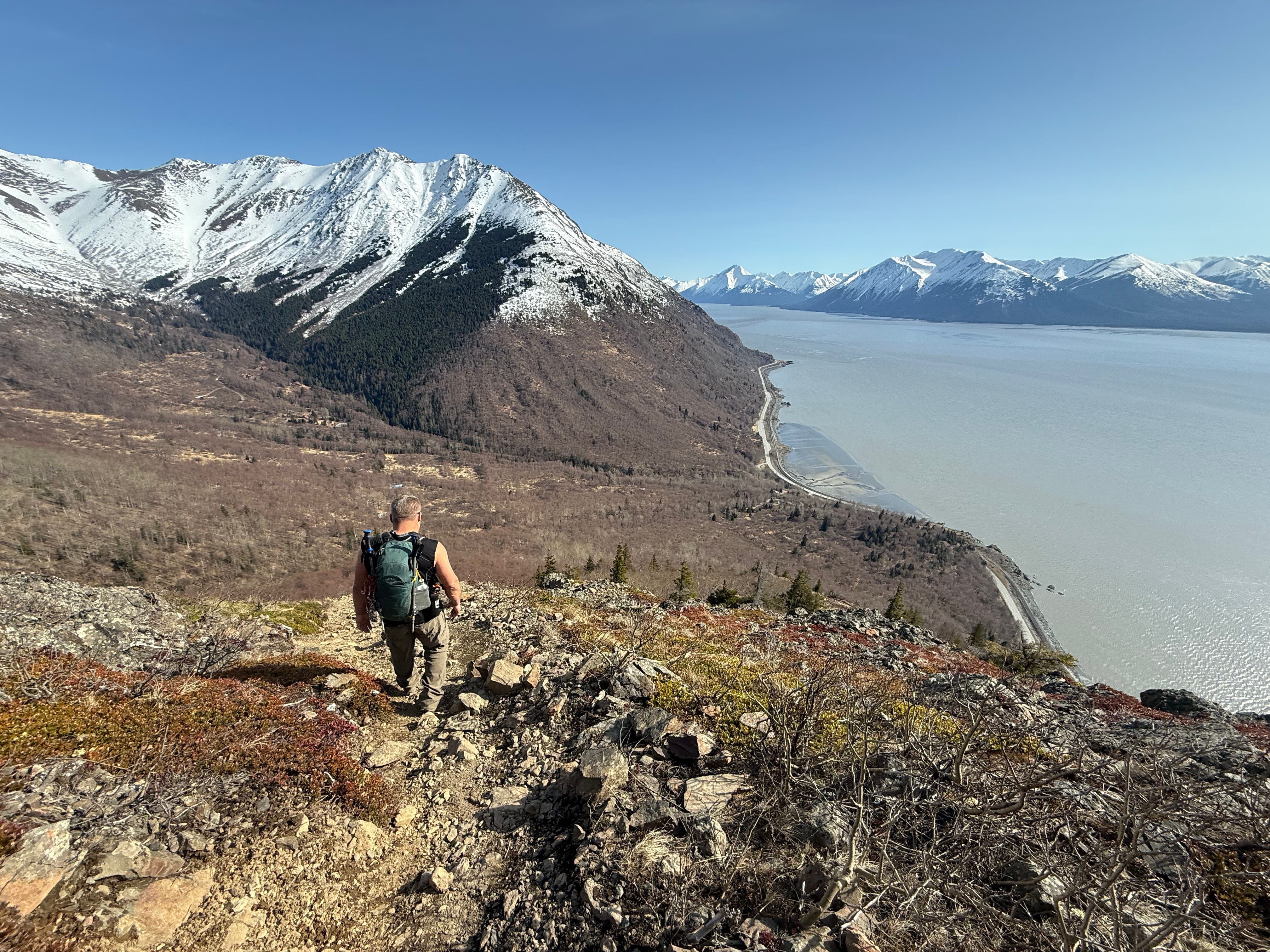 A hiker walking down a rocky path. The ocean and highway are more than 1,000' below the surface