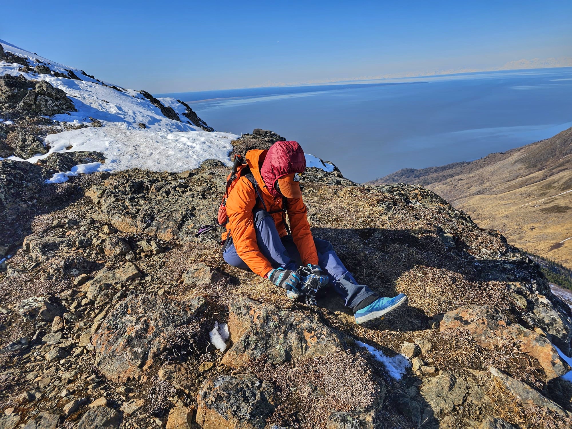 The author is wearing bright clothes while putting on microspikes. The ocean is 3500' below