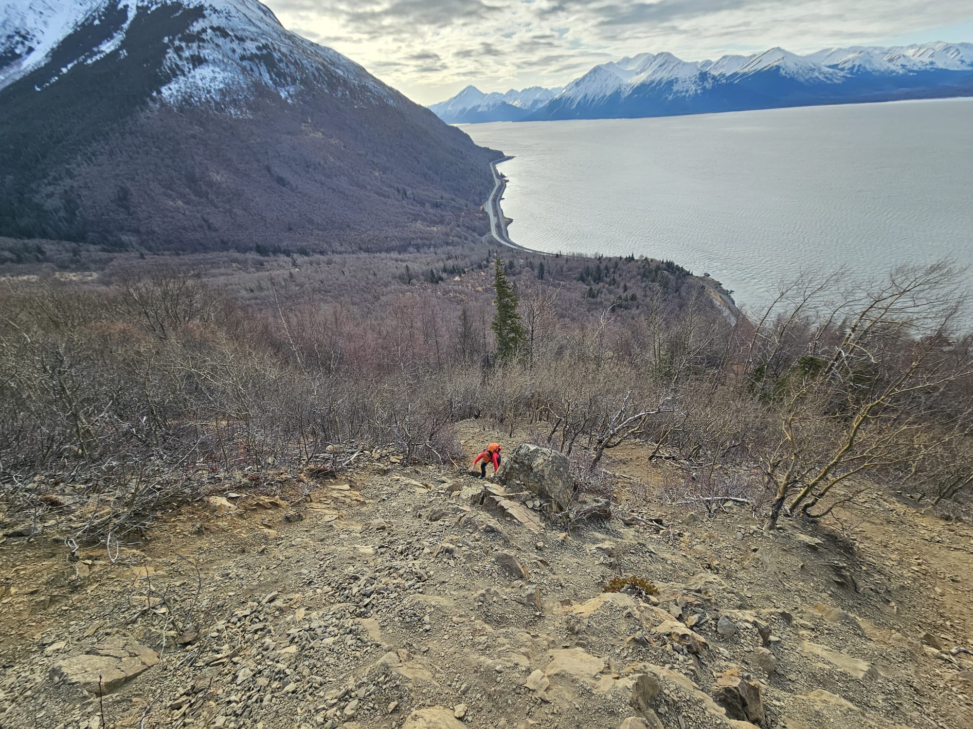 Teh author is climbing up a steep, rocky slope. The ocean and a road is visible below.